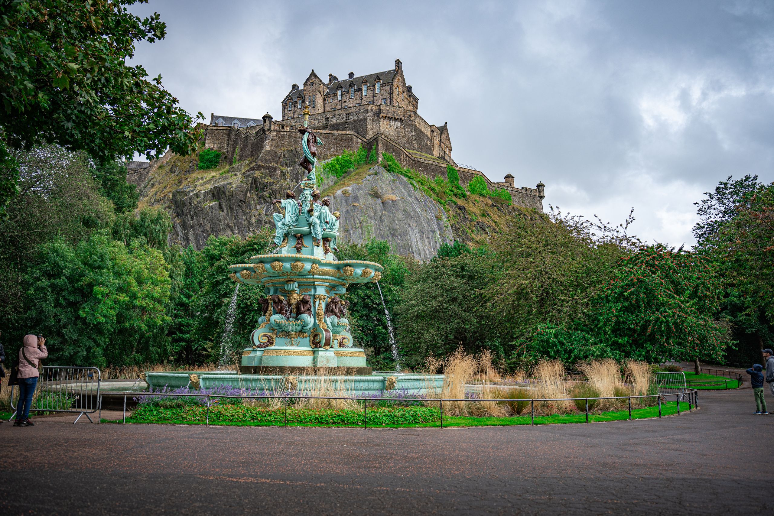 Beautiful view of Edinburgh Castle and Ross Fountain surrounded by lush greenery in Scotland.