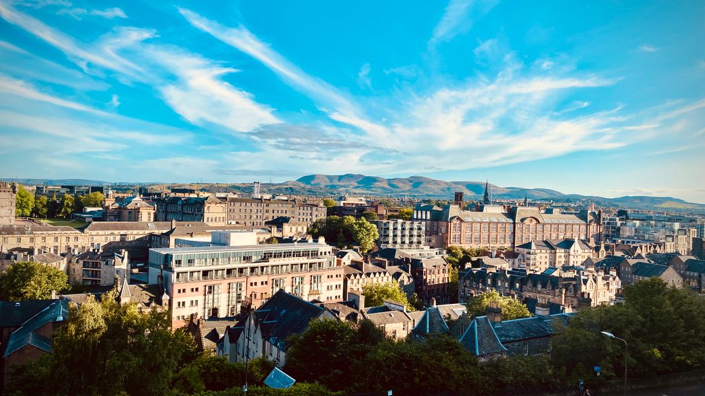 A breathtaking aerial view of Edinburgh's historic cityscape and distant hills under a bright blue sky.