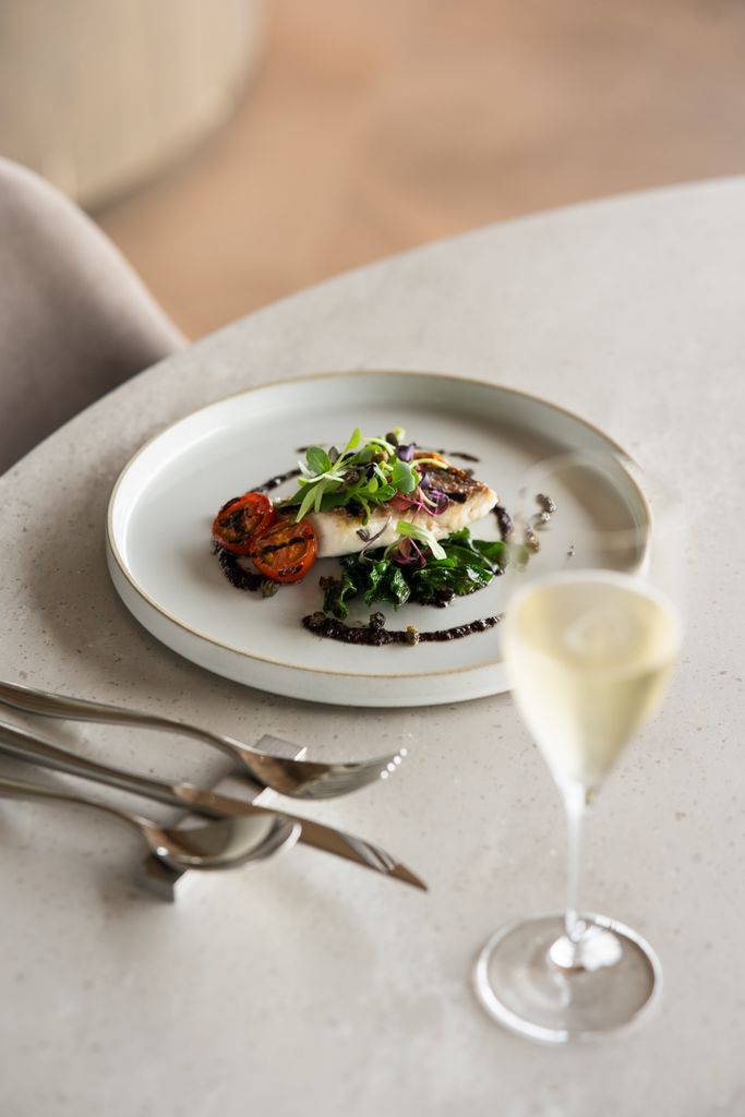Gourmet fish dish elegantly plated with tomatoes and greens, paired with champagne in a Tokyo, Japan restaurant.