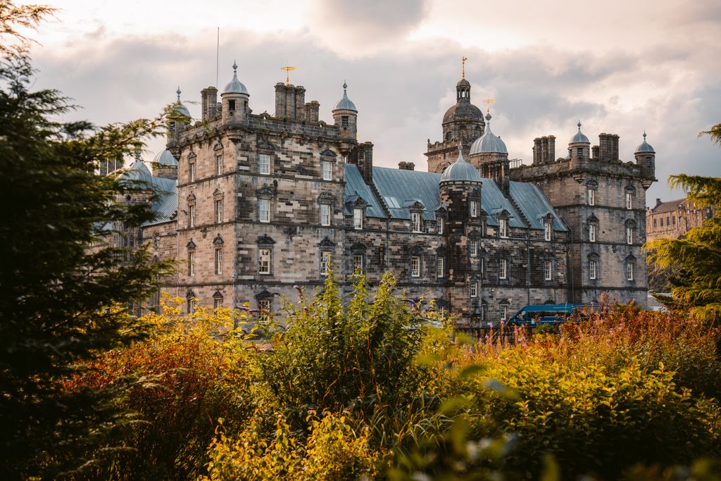 Stunning view of a historic Scottish castle framed by vibrant autumn foliage, under a cloudy sky.